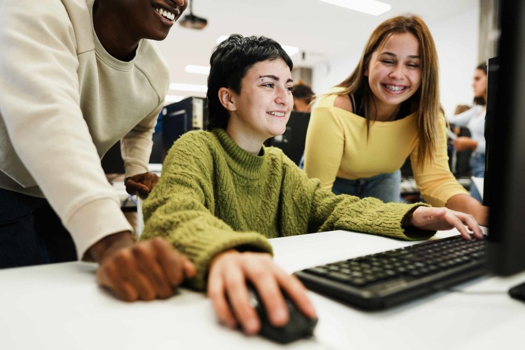 drei Jugendliche sind versammelt um einen Computer und lächeln